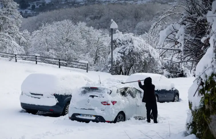 Aldeia coberta de neve, pessoa tira neve de cima dos caros.